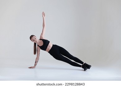 A young girl with brown hair, with a tattoo in a black top and leggings on a white background. Sports, fitness, is in the sidebar. Press exercises. Yoga