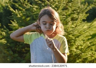 Young girl, brunette female, holding a dandelion in her hand, blowing seeds,pine tree background, upclose with sunlight. 