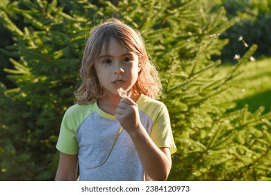 Young girl, brunette female, holding a dandelion in her hand, blowing seeds,pine tree background, upclose with sunlight. 