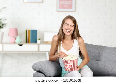 Muchacha con cubo de palomitas de maíz sentada en el sofá de su casa viendo una película