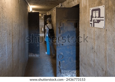 A young girl with a cap and backpack visiting the interior of the German WWII bunkers of the Museum and the Merville Battery site. Armored doors and cement and concrete walls. ammunition bunker
