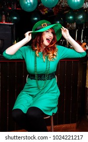 Young girl celebrate St. Patrick's Day. Woman have fun at the bar. A beautiful girl in a green leprechaun hat and dress drinks a green cocktail.