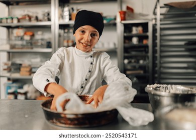 A young girl chef in a black hat and white chef uniform passionately preparing dough, utilizing professional kitchen equipment and utensils in a commercial kitchen setting. - Powered by Shutterstock