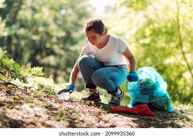 Young girl cleaning up the forest, she is collecting trash and holding a garbage bag, environmental protection concept