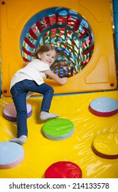 Young Girl Climbing Up Ramp Into Tunnel At Soft Play Centre