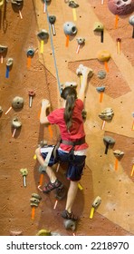 A Young Girl Climbing A Tall, Indoor, Man-made Rock Climbing Wall