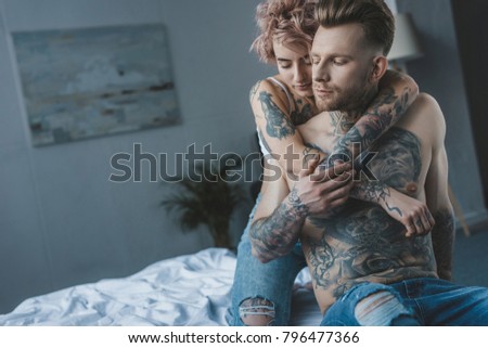young girl with closed eyes hugging her tattooed boyfriend in bed