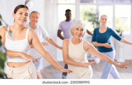 Young girl coach conducts classes for elderly in fitness studio. Female instructor teaches mature students of dance class basic movements of hip hop dance - Powered by Shutterstock