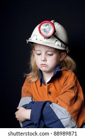 Young Girl In Coal Miner Hard Hat And Safety Clothing, Looking Sad, Black Background