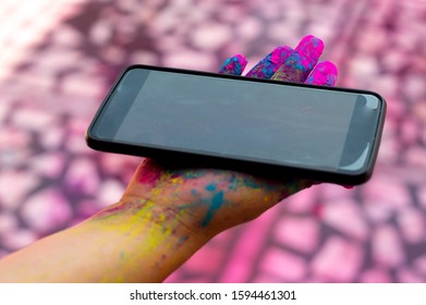 Young Girl With Colored Gulaal Powder On Her Hands Holding A Mobile Phone During The Festival Of Holi. Shows The Inclusion Of Social Media And Digital Devices That Are Waterproof And Powder Proof