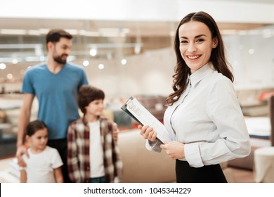 Young Girl Consultant Demonstrates Orthopedic Mattress To Young Father With Children In Furniture Store. Purchase Of Orthopedic Mattress. Sale Of Orthopedic Mattress In Furniture Store.