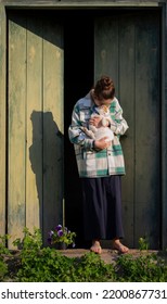 Young Girl In The Countryside In Summer. White-red Cat Is In Her Hands. In The Background Are Large Green Wooden Doors. Girl Stands Barefeet. Beautiful Young Woman Outdoors. Vacation In The Village.