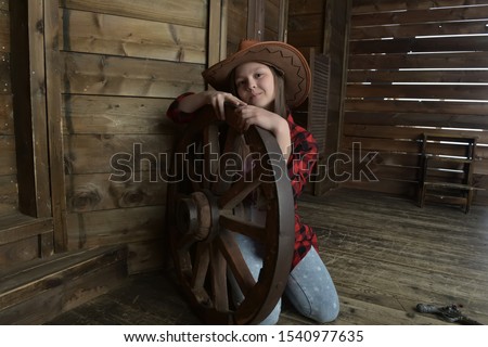young girl cowboy in a red checkered shirt on the background of a wooden wall