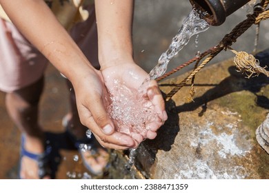 A young girl cradles refreshing water in her hands, poised to quench her thirst.
