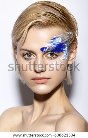 Young girl with creative makeup and textures on her face. Beautiful model with  blue and white pigment in studio, on white background