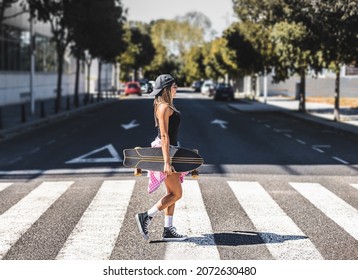 a young girl crosses a crosswalk with a skateboard in her hand. cityscape concept.