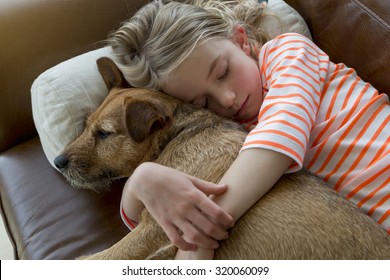 Young girl cuddling her pet dog on a sofa at home.