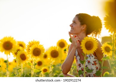 Young girl with curly hair in the middle of a field of sunflowers at dusk. - Shutterstock ID 1902912274