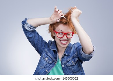 Young Girl Cut Hair With Scissors With Mad Eyes. Bad Day At The Hairdresser.Studio Shot. Gray Background