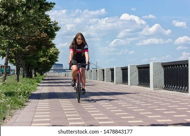 A young girl cyclist in cycling clothes rides along a long promenade on a sports red cycling bike. - Shutterstock ID 1478843177