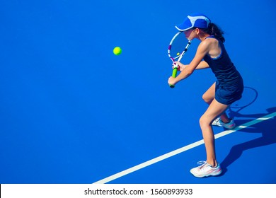 young girl in a dark blue dress plays tennis on the court with a hard coating of blue