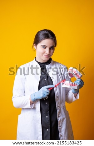 Young girl doctor in black medical uniform cleans the mould of jaws with a toothbrush on a yellow background