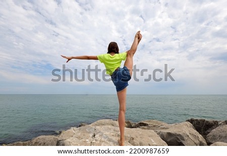 young girl does gymnastic exercises to train her balance by stretching herself on a single leg on the rocks of the rocks by the sea