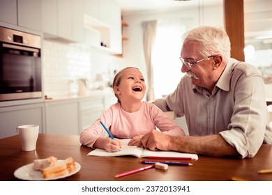 Young girl doing homework with the help of her grandfather at home - Powered by Shutterstock