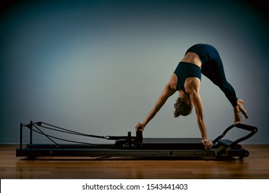 Young girl doing pilates exercises with a reformer bed. Beautiful slim fitness trainer on a reformer gray background, low key, art light, copy space advertising banner - Powered by Shutterstock