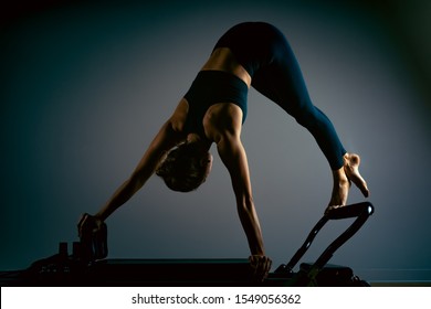 Young girl doing pilates exercises with a reformer bed. Beautiful slim fitness trainer on reformer gray background, low key, art light. Fitness concept - Shutterstock ID 1549056362