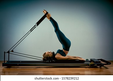 Young girl doing pilates exercises with a reformer bed. Beautiful slim fitness trainer on reformer gray background, low key, art light. Fitness concept - Shutterstock ID 1578239212