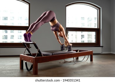 Young girl doing pilates exercises with a reformer bed. Beautiful slim fitness trainer on reformer gray background, low key, art light. Fitness concept - Powered by Shutterstock