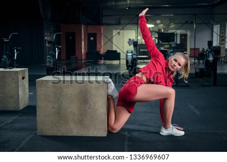 Young girl doing yoga on the floor at gym. Standing in a pose on one knee, having bent a leg. Gripping the foot with hand behind
