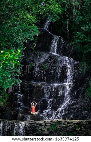 young girl doing yoga in the wild inside a waterfall of water on spring sunny day