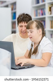 Young Girl With Down Syndrome  Uses A Laptop With Her Teacher At Library. Education For Disabled Children Concept