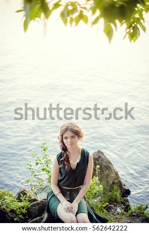 Young girl in dress sitting on rocks near water