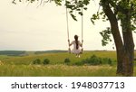 A young girl in dress swinging on swing in evening park. Wooden swing with swinging free, happy woman outdoors. Swing on a swing, dreams of flying. Travel in spring summer in nature. Healthy lifestyle