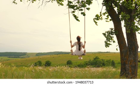 A young girl in dress swinging on swing in evening park. Wooden swing with swinging free, happy woman outdoors. Swing on a swing, dreams of flying. Travel in spring summer in nature. Healthy lifestyle - Powered by Shutterstock