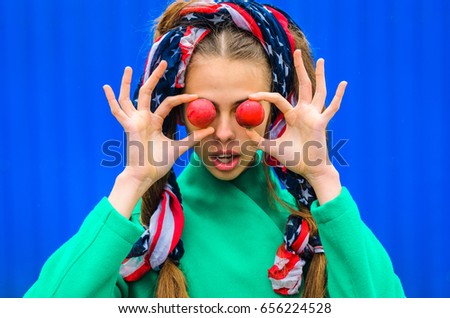 a young girl dressed in a green coat and yellow dress. Pure colors in the photo. girl fun fooling around .hair America flag in the hands of the red halves of the fruit , close your eyes and laugh