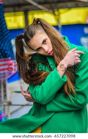 a young girl dressed in a green coat and yellow dress. Pure colors in the photo. girl fun fooling around . the grey shelves, the girl in the yellow truck . is there  American flag.