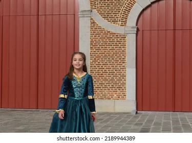 A young girl dressed in medieval garb stands before a castle - Shutterstock ID 2189944389