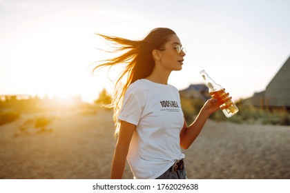 Young girl drinking beer from a bottle on the beach at sunset during summer vacation. Summer holidays, relax and lifestyle concept.