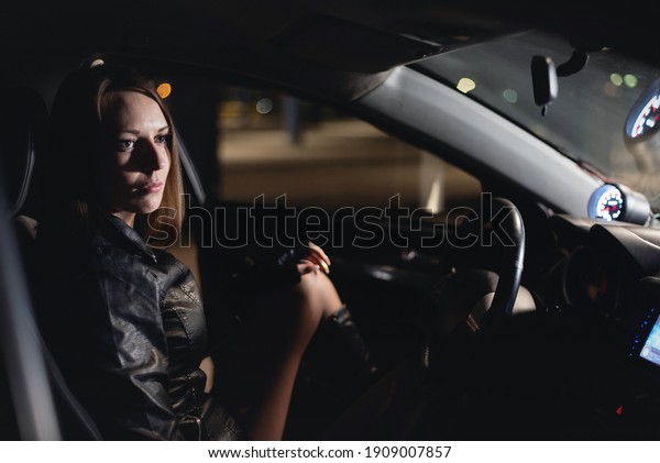 Young girl a driver in shorts and black leather\
jacket is sitting on the car\
seat.