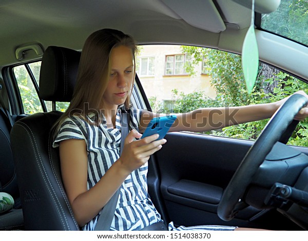 young\
girl driving a car with a mobile phone in her\
hand