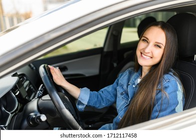 A young girl driving a car. She is in casual jeans jacket looks at camera and smiles