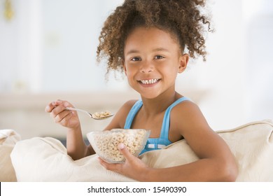 Young Girl Eating Cereal In Living Room Smiling