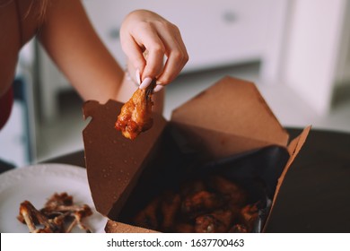 Young Girl Is Eating Chicken Wings From A Takeout Container At Home