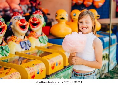Young girl eating cotton candy fairy floss at a carnival fairground in front of clowns
