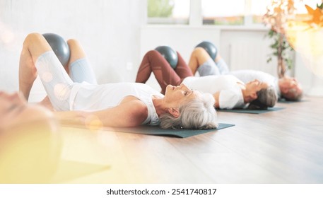 Young girl with elderly colleagues doing Pilates in studio. People lie on karemat, raised bent legs to stomach and hold soft ball in knees - Powered by Shutterstock