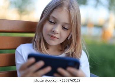 A young girl engrossed with her smartphone, enjoying technology and outdoor play in a summer park. - Powered by Shutterstock